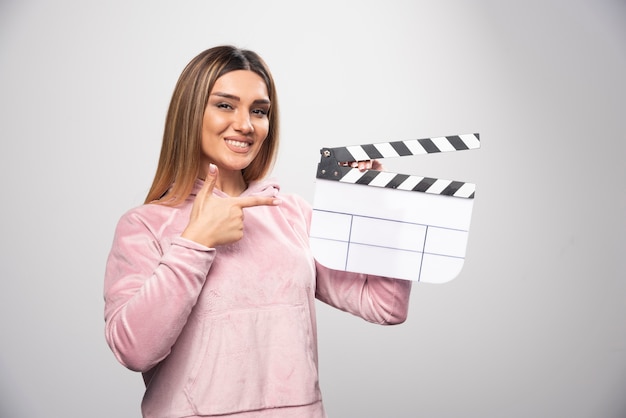 Blond lady in pink sweatshier holding a blank clapper board and gives natural poses.