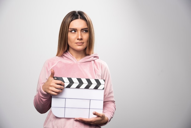 Blond lady in pink sweatshier holding a blank clapper board and gives natural poses