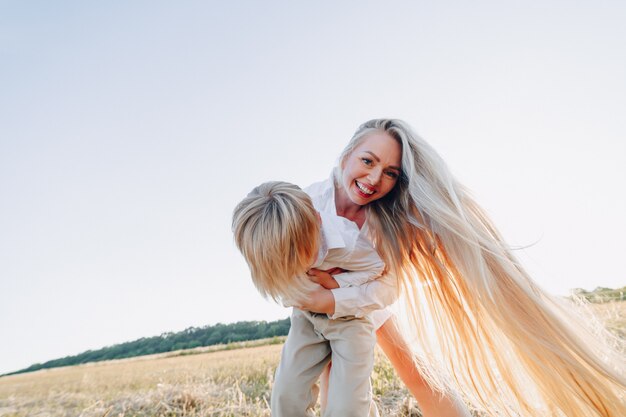 Blond little boy playing with mom with white hair with hay in field. summer, sunny weather, farming. happy childhood.