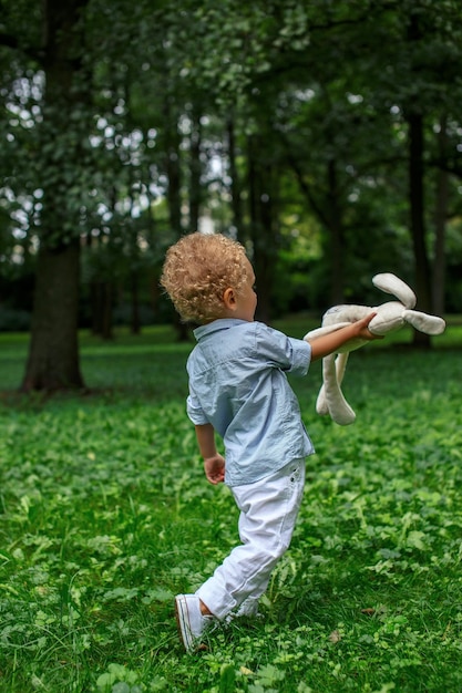 A blond little child boy playing green park.