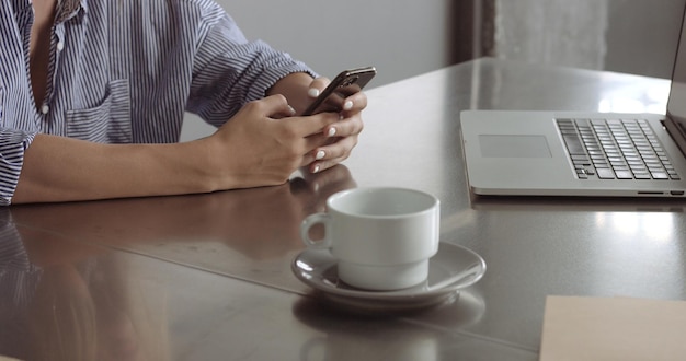 Blond model in a relaxed buttonup shirt switches between her laptop and her phone at work