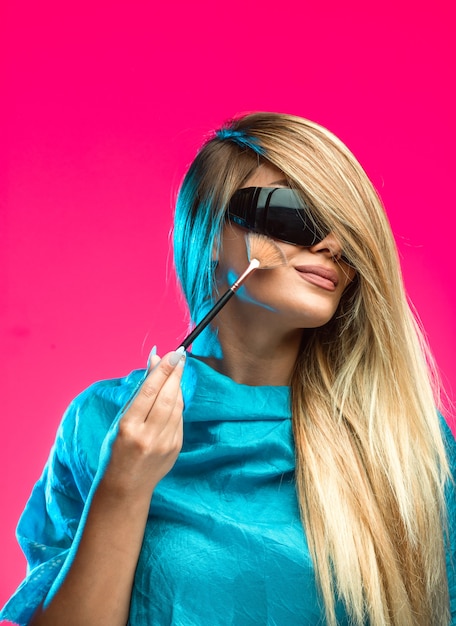 Free photo blond model wearing black sunglasses and applying cosmetics.