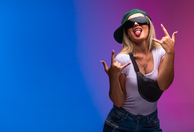 Free photo blond model wearing green cap and sunglasses with tongue out.