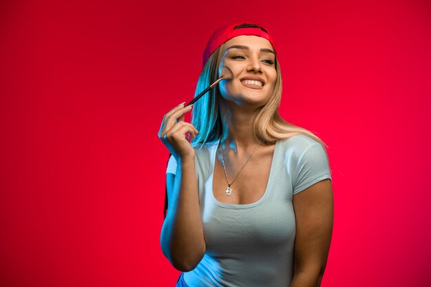 Blond model wearing red cap and applying makeup. 