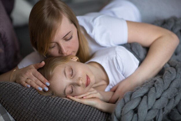 Blond mom and daughter teenager sleep hug on bed