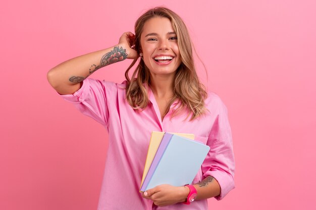 ノートブックを保持している笑顔のピンクのシャツを着た金髪のきれいな女性