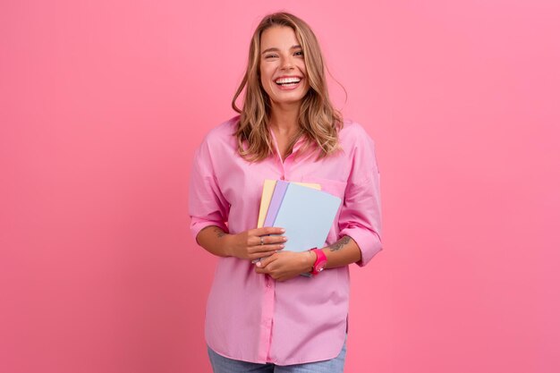 持っているノートを持って笑っているピンクのシャツを着た金髪のきれいな女性