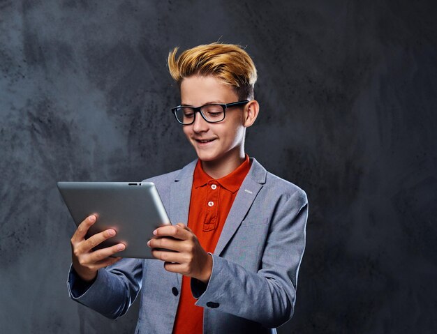 Free photo blond schooler boy in eyeglasses holds tablet pc.