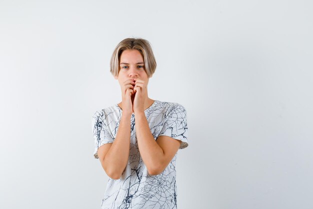 The blond teenage boy is thinking by covering his mouth with fists on white background