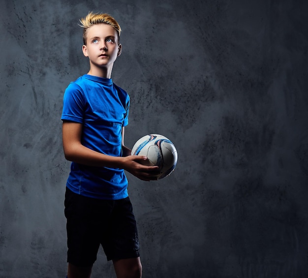 Блондинка-подросток, футболист, одетый в синюю форму, держит мяч.