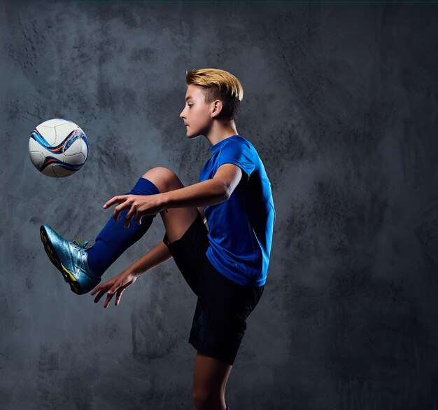 금발의 십대, 파란색 유니폼을 입은 축구 선수가 공을 가지고 노는다.