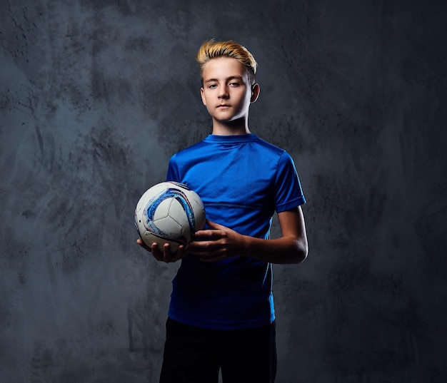 Free photo blond teenager, soccer player dressed in a blue uniform plays with a ball.