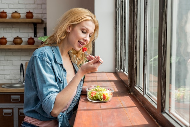 Белокурая женщина ест салат