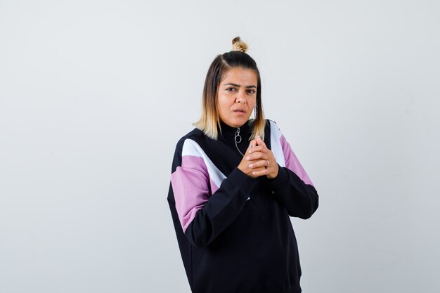 Blond woman holding hands in front of herself, standing sideways in black tracksuit and looking troubled .