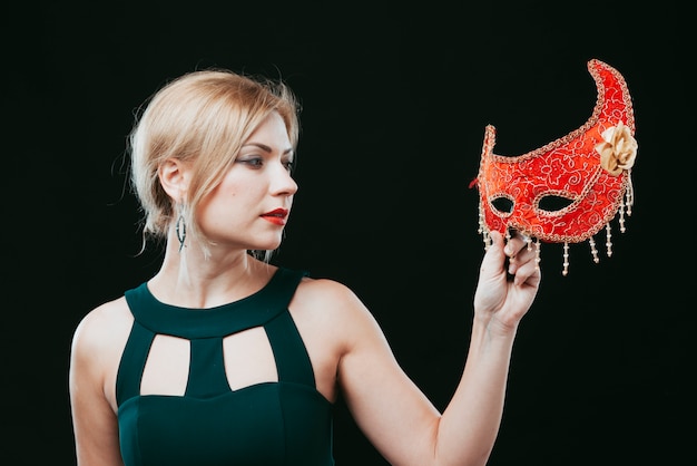 Бесплатное фото Белокурая женщина смотрит на красную карнавальную маску