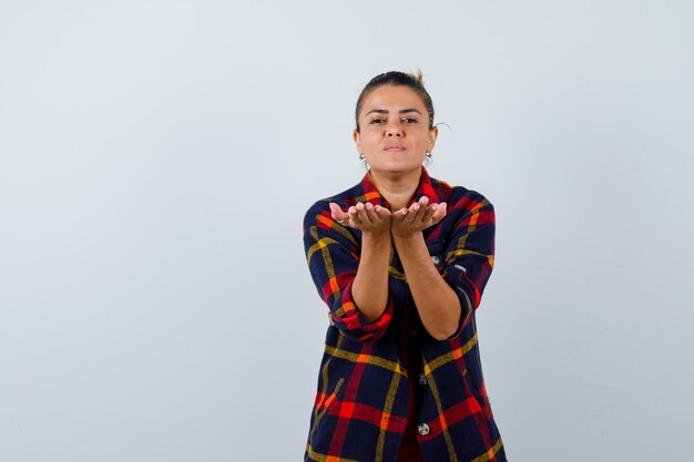 Free photo blond woman making giving gesture in checkered shirt and looking peaceful , front view.