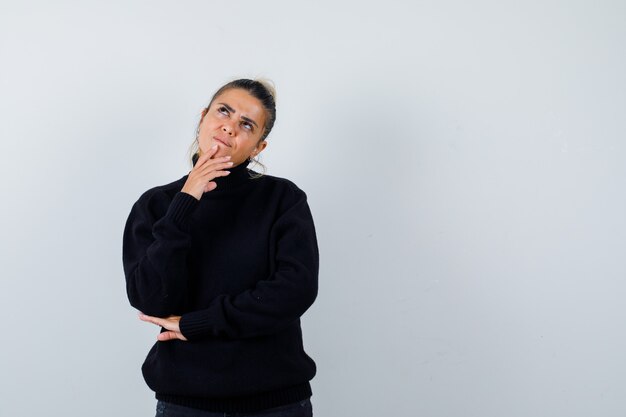 Blond woman standing in thinking pose in black sweater and looking sensible , front view.