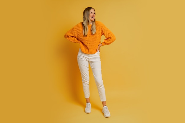 Foto gratuita donna bionda con la faccia di suprice in maglione autunnale alla moda arancione in posa sul giallo. intera lunghezza.