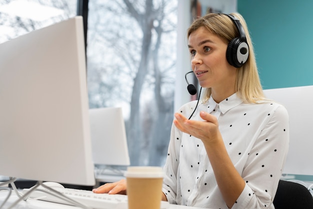 Blond woman working in a call center with headphones and computer