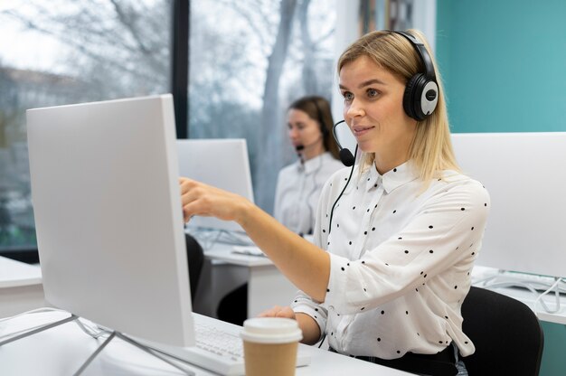Blond woman working in a call center with headphones and computer