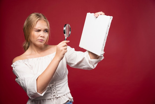 Free photo blonde art master checking the canvas with a magnifier and looks doubtful.