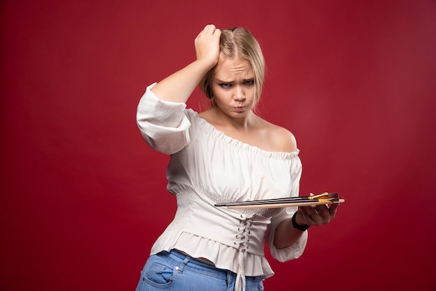 Blonde artist holds a palette and brushes and looks surprized and confused.