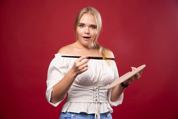 Blonde artist holds a palette and brushes and looks surprizingly positive.