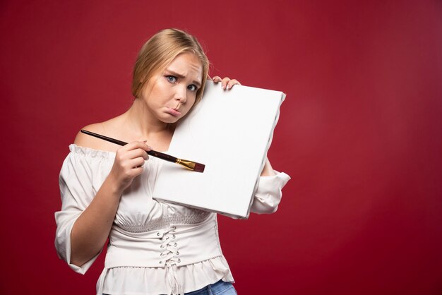 Blonde artist showing her artwork and looks doubtful.