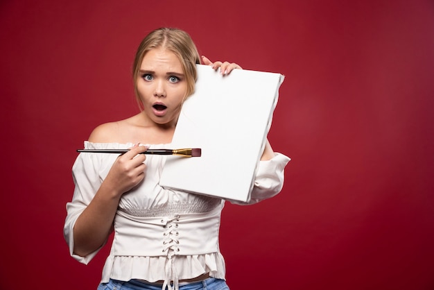 Blonde artist showing her artwork and looks doubtful.