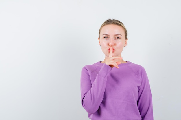 The blonde beautiful girl is holding her forefinger on lips on white background