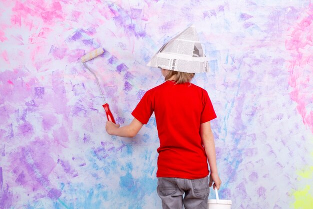 blonde boy back view in red t-shirt and grey jeans painting colorful walls