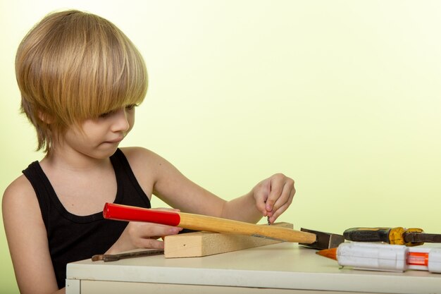 blonde boy in black t-shirt working with hammer and other tools on white wall