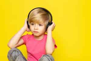 Free photo blonde boy in pink t-shirt and grey jeans in black earphones listening to music