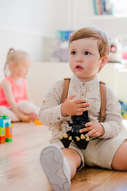 Blonde boy sitting holding dinosaur toy staring