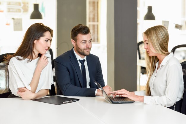 Blonde businesswoman explaining with laptop to smiling young cou