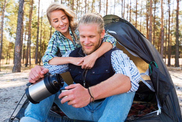 Blonde couple sitting in front of tent and drinking coffee