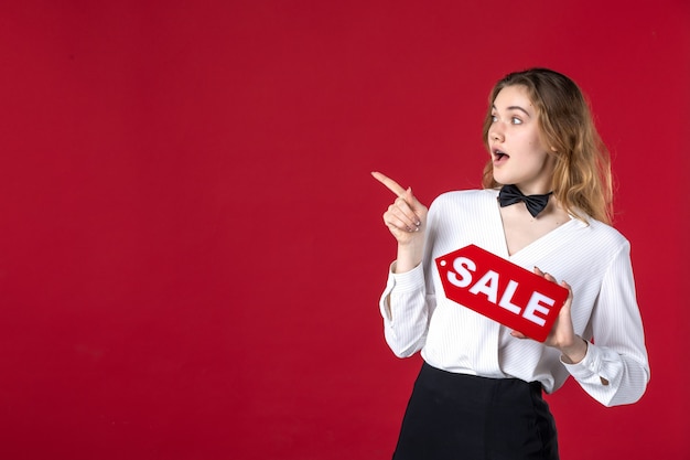 Free photo blonde curious female server butterfly on the neck and holding sale icon pointing something on the right side on red background