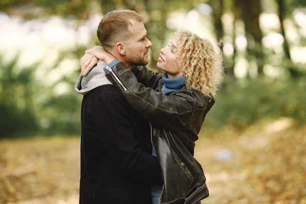 Blonde curly woman and man standing in autumn forest and hugging