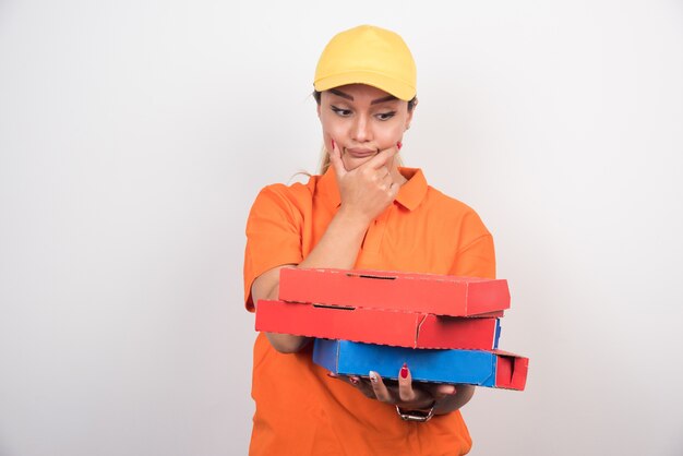 Blonde delivery woman holding pizza boxes on white space while thinking about something