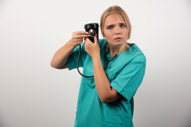 Blonde doctor holding cup of coffee with scared expression.