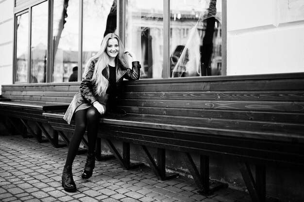 ベンチに座っている長い黒革のコートで金髪のファッショナブルな女の子