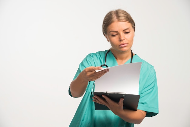 Блондинка женщина-врач в синей форме проверяет историю болезни пациента.