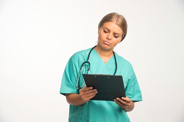 영수증 책을 들고 조심스럽게 그것을 확인하는 파란색 유니폼에 금발 여성 의사.