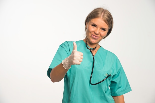 Free photo blonde female doctor in blue uniform with stethoscope in the neck making positive sign.