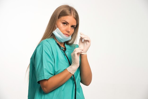 Blonde female doctor in face mask wearing hand gloves. 