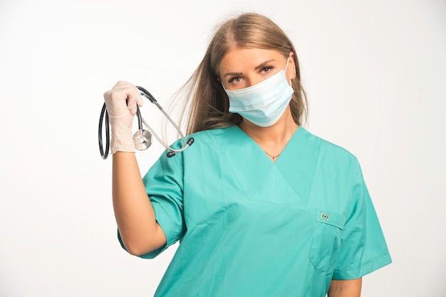 Blonde female doctor wearing face mask and holding a stethoscope .
