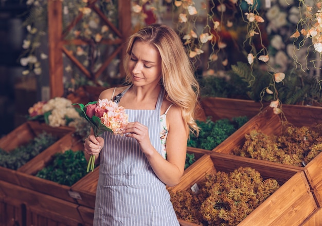 Blonde female florist looking at bouquet standing in front of wooden crate