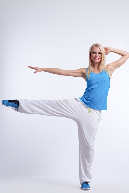 blonde female in hip hop dancing outfit balancing on one leg smiling on white