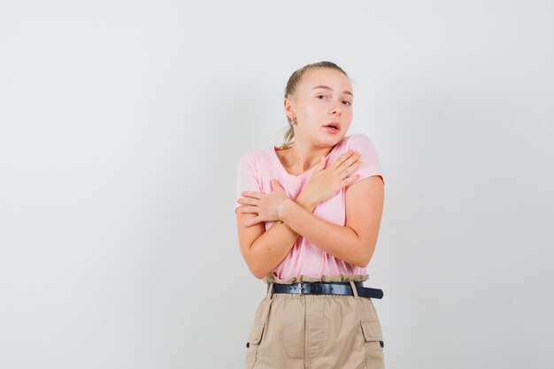 Blonde female holding crossed hands on chest in t-shirt, pants and looking elegant , front view.