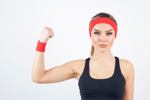 Blonde fit woman in black sportswear standing and showing biceps.  